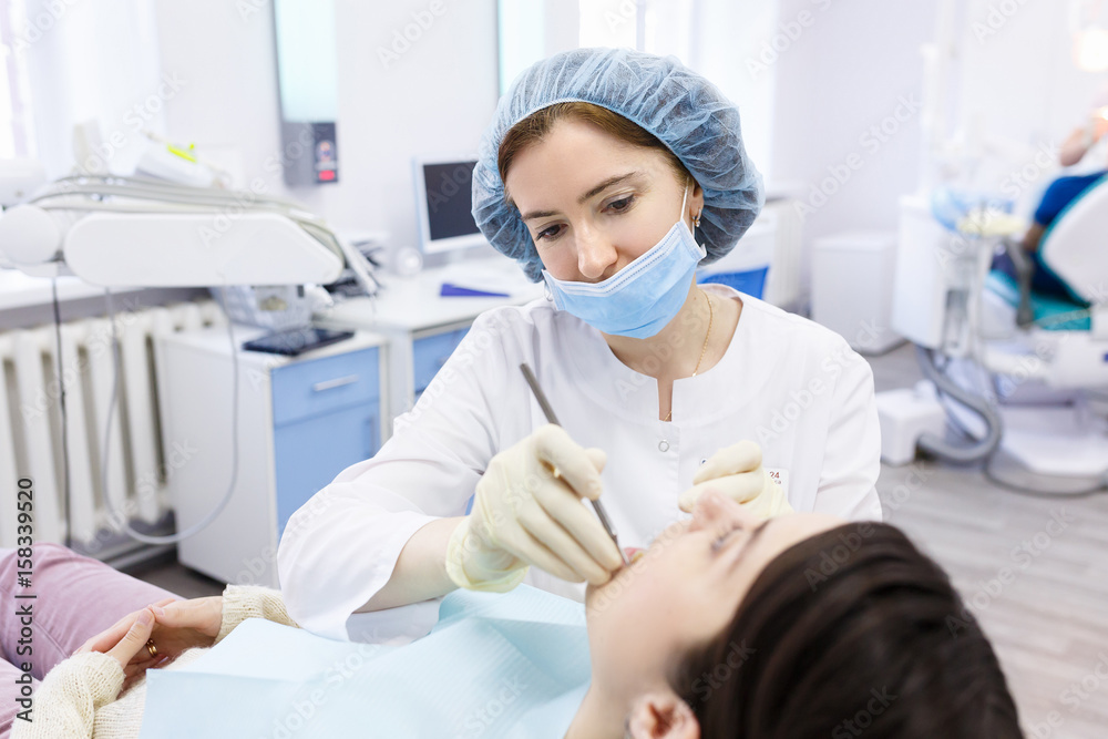 Young female patient in dentist office. Dentist examines the patient teeth at dental chair with open mouth, dental procedure in clinic Young female patient in dentist office. Dentist examines the patient teeth at dental chair with open mouth, dental procedure in clinic