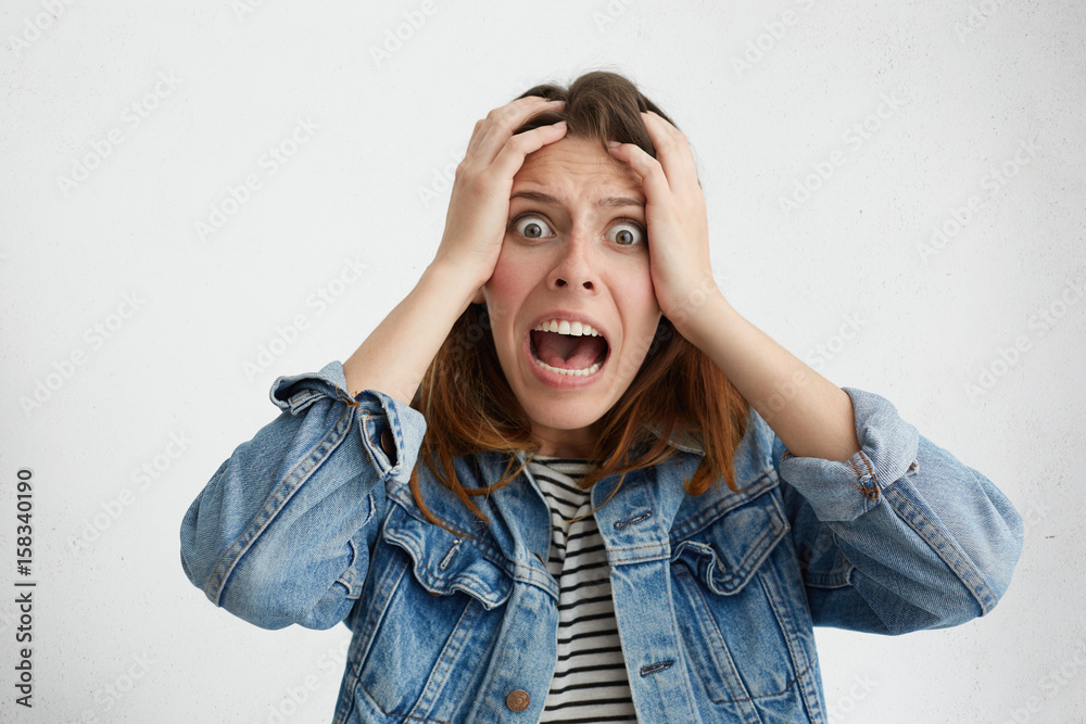 Shocked panic Caucasian girl dressed in stylish clothing holding hands on head and screaming in despair and frustration while being late for plane, her eyes full of terror, mouth dropped open Shocked panic Caucasian girl dressed in stylish clothing holding hands on head and screaming in despair and frustration while being late for plane, her eyes full of terror, mouth dropped open