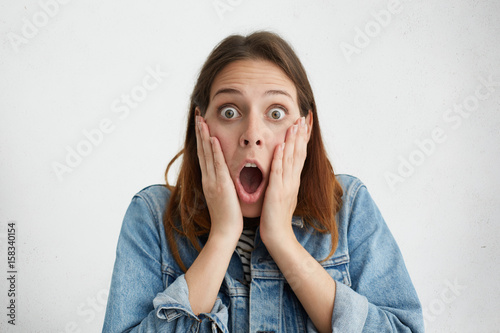 Funny woman customer wearing denim jacket holding hands on cheeks and screaming in full desbelief, keeping mouth wide opened and eyes popped out, having shocked look because of big sale prices