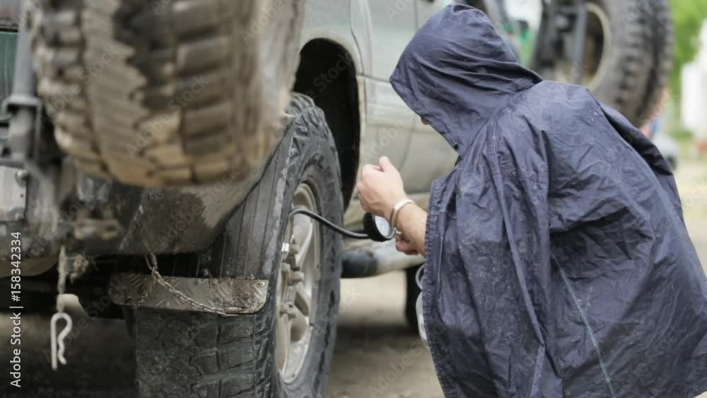 Man in raincoat pumping wheels of SUV at roadside Man in raincoat pumping wheels of SUV at roadside