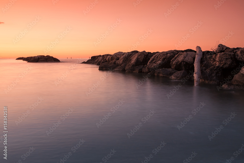 Orange sunset in front of the sea and stones in the water