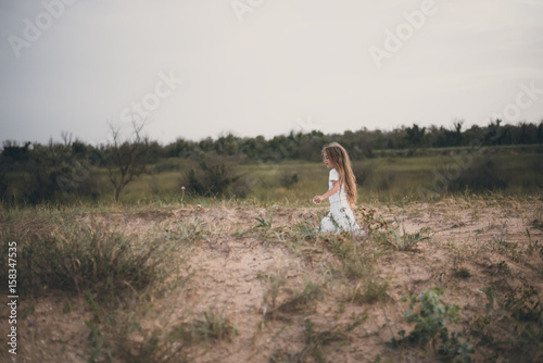 Blurred image Copy space Background Long-haired girl in white clothes Lonely runs Desert sand field near forest at sunset down. Selective focus. Toned image