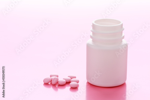 A white plastic bottle of drugs and a pile of pink pills