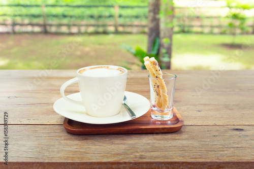 Coffee cup and pastry on wooden table with nature background.