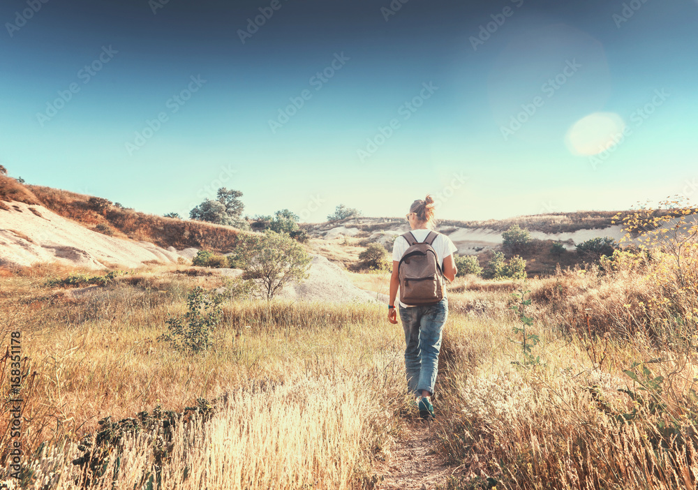 The girl with a backpack walks the field in the rays of the setting sun. Beautiful landscape, freedom, the unity of human and nature The girl with a backpack walks the field in the rays of the setting sun. Beautiful landscape, freedom, the unity of human and nature