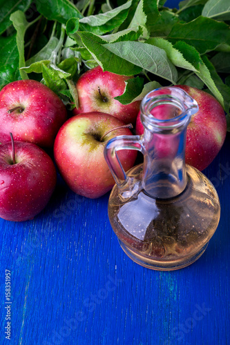 Apple cider vinegar. One glass bottle on blue background. Red apples.