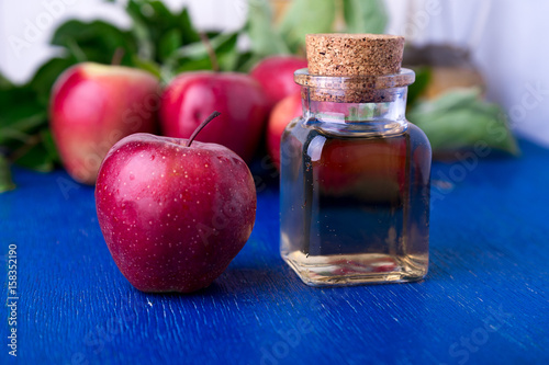 Apple cider vinegar. One glass bottle on blue background. Red apples.