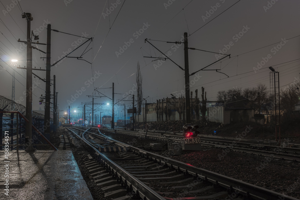 Plehanovskaya station in Voronezh, Russia. Railway station in the night, bad weather, rails and wires under the cloudy sky. Red railway signals between the rails.