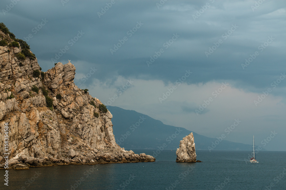 The Sail rock, Gaspra, Crimea, Russia. A rock in the Black sea, a yacht near it, and the eagle statue over it. A cloudy sky at the background.