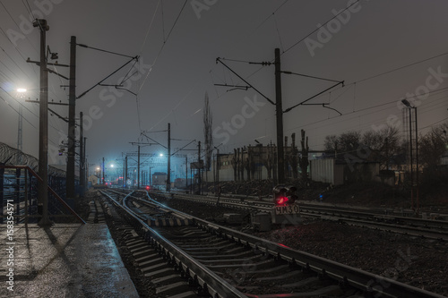 Plehanovskaya station in Voronezh, Russia. Railway station in the night, bad weather, rails and wires under the cloudy sky. Red railway signals between the rails.
