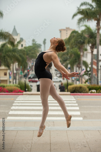 Beautiful and young ballerina leaping to left above downtown Ventura with both legs forward. 