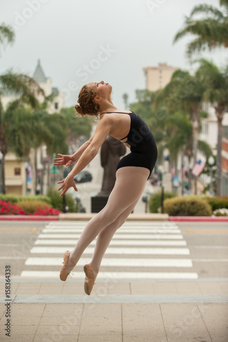 Beautiful and young ballerina leaping to right above downtown Ventura with both legs forward. 