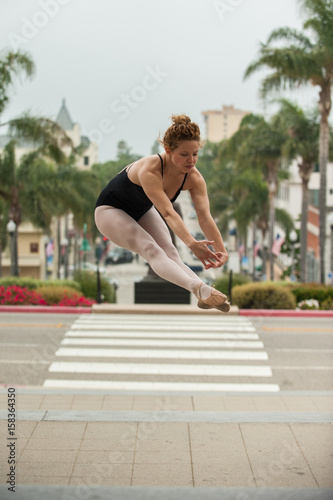Beautiful and young ballerina leaping above downtown Ventura with both legs forward. 