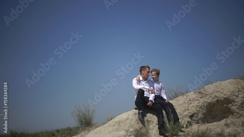 Father and son are sitting on the hill and talking about life, dreaming about the happy future of the family, about friendship and freedom, father's day