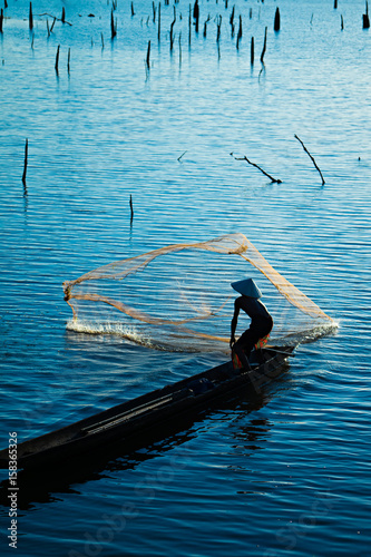 Silhouette of Fisherman catching fish in lake by using fishing net at beautiful sunset time. © thekob5123