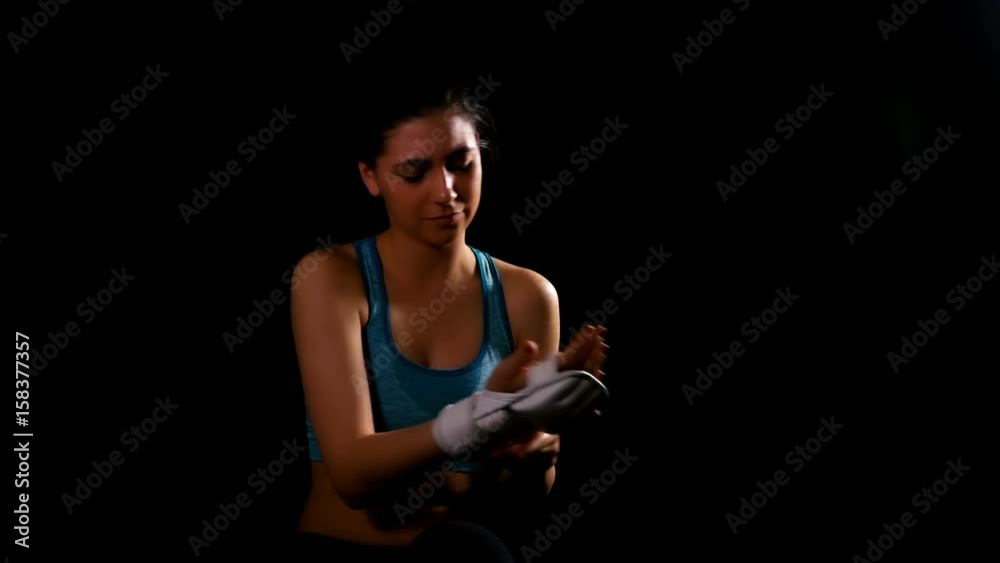 Young woman exercising boxing kicking training getting off gloves on black background Young woman exercising boxing kicking training getting off gloves on black background