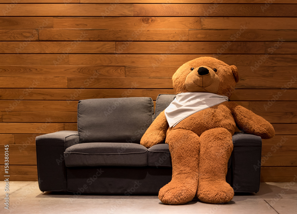 Big Bear sitting on a black sofa. And the backdrop is a wooden floor. Stock  Photo | Adobe Stock