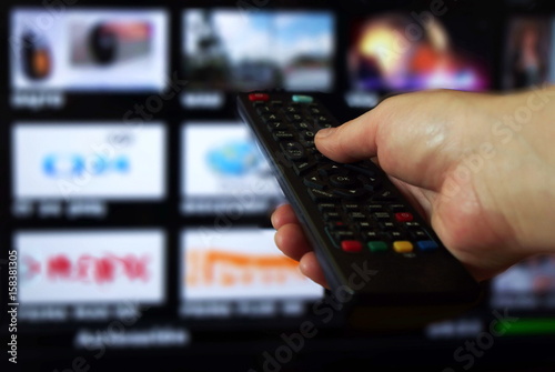 Smart tv and hand pressing remote control.Hand holding TV remote control with a television in the background. Close up.