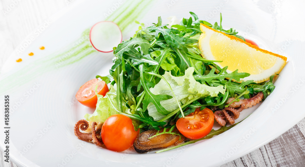 Seafood salad with mussels, squids, octopus, arugula, lettuce and cherry tomatoes on wooden background close up. Mediterranean food