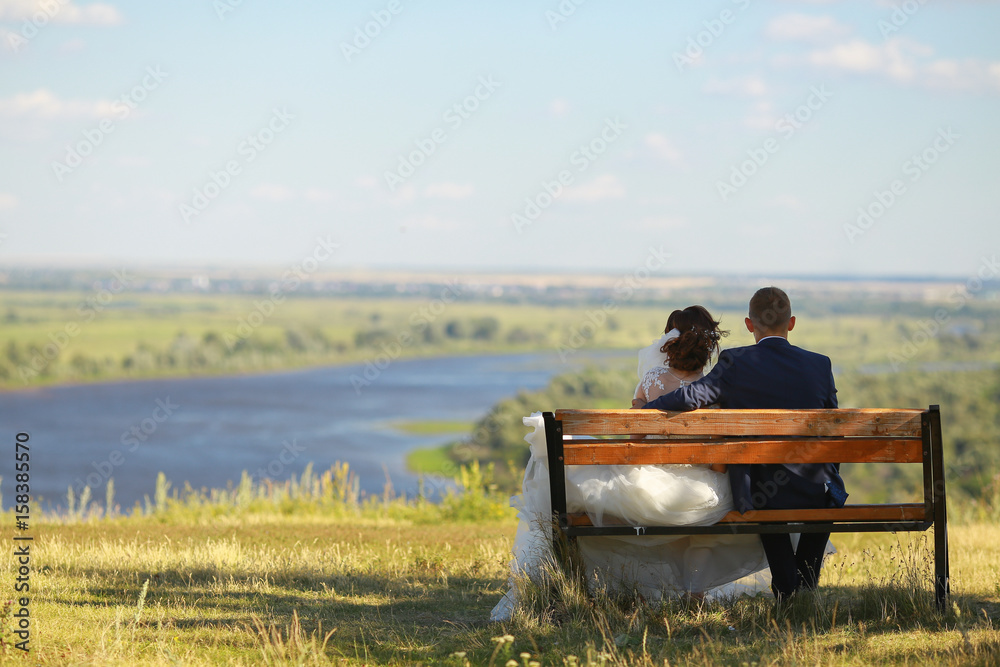 Fototapeta premium Young wedding romantic couple sitting on wooden bench outdoor on river background.