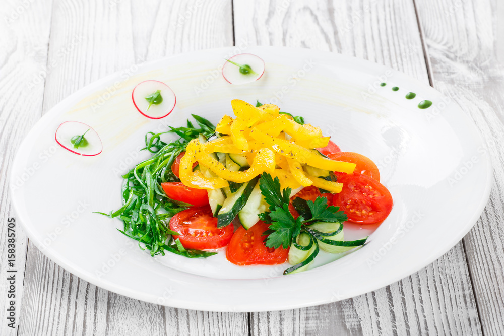 Fresh salad with cherry tomatoes, cucumber, radish, sweet pepper and onion in a plate on wooden background close up. Top view