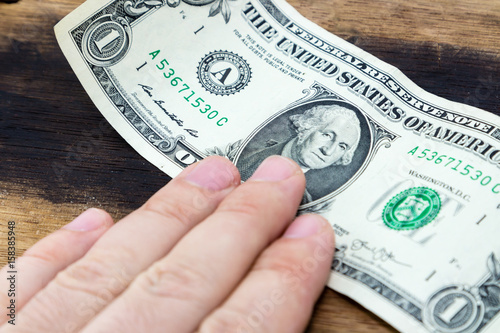 A human hand touching a one dollar USA note on a wooden table top. This image can be used to represent payment.