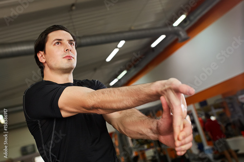 Young sporty man in the black sportwear stretching arm before gym workout.