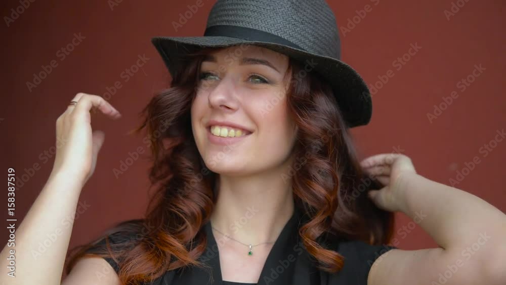 Beautiful young girl in a straw black hat playing with red hair smiling, laughing and making a face. On a red background. Beautiful young girl in a straw black hat playing with red hair smiling, laughing and making a face. On a red background.