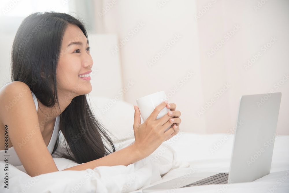 Happiness Asian girl smiling and holding cup of coffee with laptop on her bed. Happiness Asian girl smiling and holding cup of coffee with laptop on her bed.