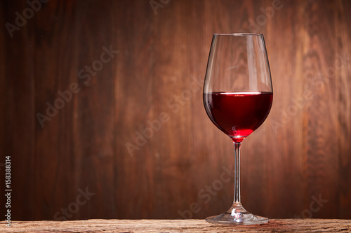 Red wine in the pure elegant wineglass standing on a wooden stand against wooden background.