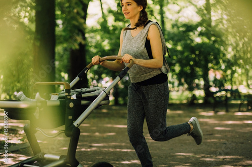 Young beautiful sporty mother jogging and pushing baby stroller in sunny summer day.