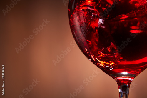 Close-up of the abstract splashing of the red wine in the fragile wineglass on the brown wooden background.