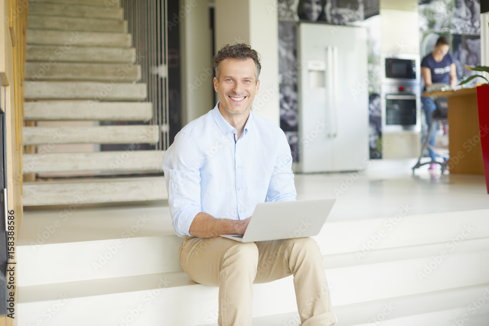 Manage my business from home. Shot of a smiling casual man using his laptop and working online while sitting on stairs at his modern home. 