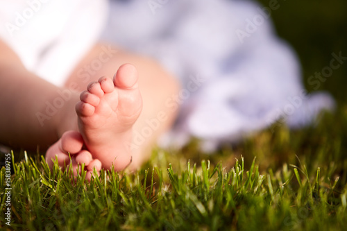 Close-up of little baby feet on green grass outdoors in the city park.