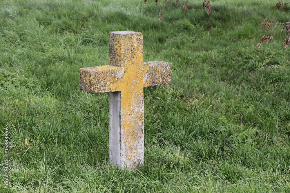 An old cross on a grave overgrown with grass in a cemetery