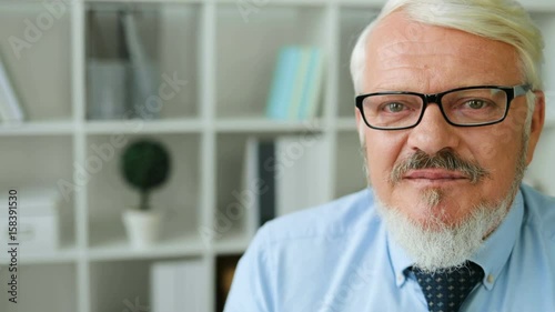 Portrait of midle aged business man in glasses looking to side, turning and posing to the camera and smiling on office background. photo