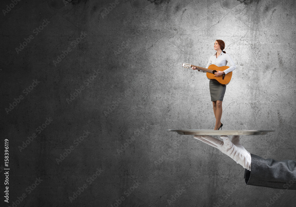 Attractive businesswoman on metal tray playing acoustic guitar against concrete wall background