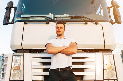 Portrait of Young Muscular Man Driver in White T-shirt Standing Near Truck, Trucker Concept photo