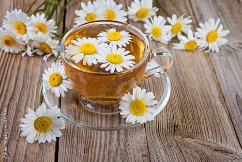 cup of camomile tea and  camomile flowers on wooden background