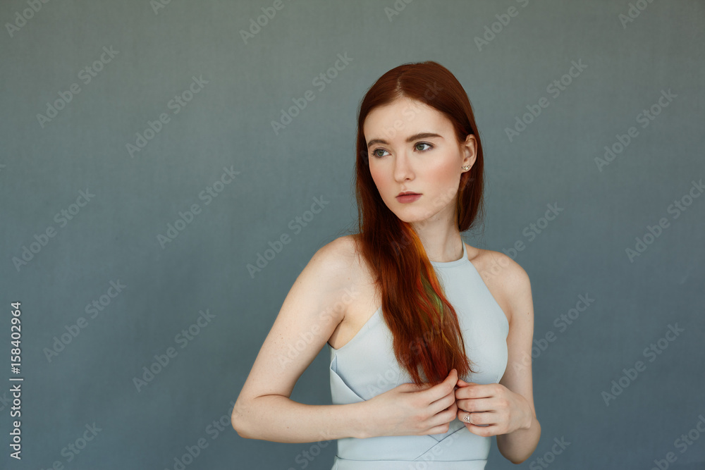 Portrait of the beautiful female model with red long hair and gorgeous green eyes against blue brick wall in studio. Attractive young woman looking away with thoughtful and dreamy expression