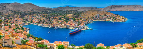 Panoramic view on beautiful Symi island Aegean Sea blue bay Greek houses on green hills, yacht sea port, tourist ferryboat. Famous Mediterranean MSC cruises. Greece islands holiday vacation tours trip photo