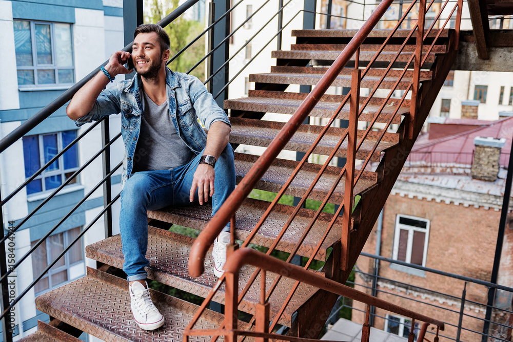 Joyful guy speaking by cellphone on stairs Joyful guy speaking by cellphone on stairs