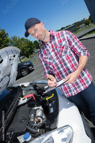 Man with clipboard looking at vehicle engine © auremar