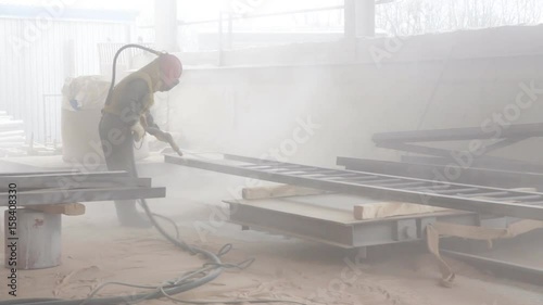 Worker sandblasting metal construction by sandblaster photo