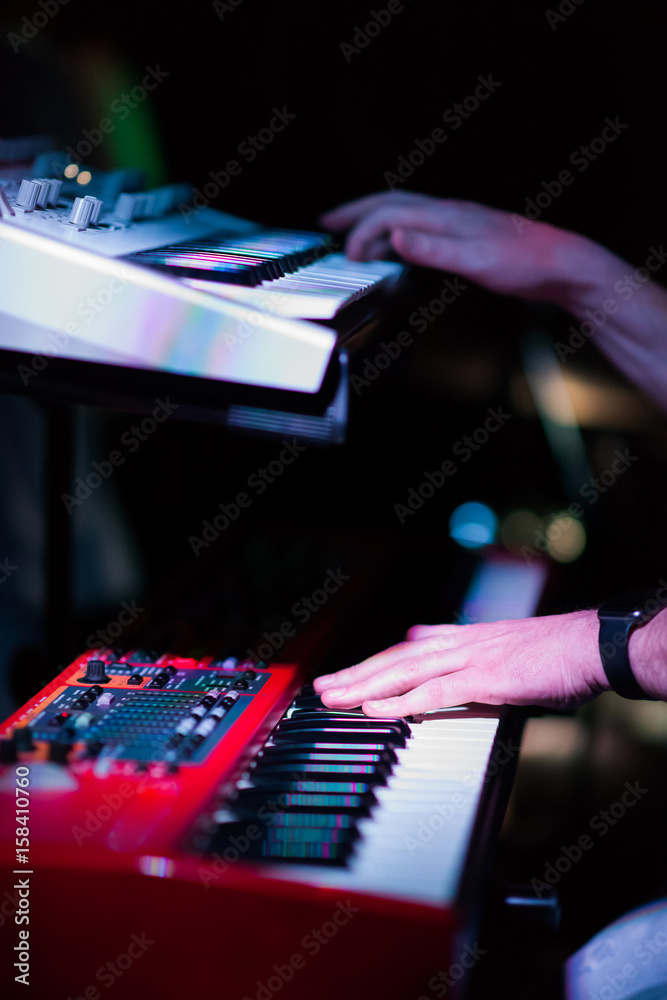 Musician playing on the double keyboard synthesizer piano keys. Musician plays a musical instrument on the concert stage Musician playing on the double keyboard synthesizer piano keys. Musician plays a musical instrument on the concert stage