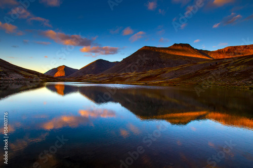 Mountain lake at sunset of the day. Mountains against the background of the evening sky. The pond in the mountains. Stones in the water. Reflection in water.