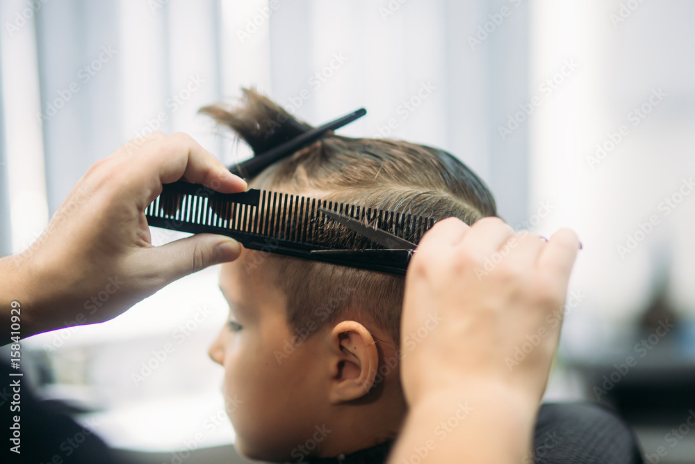 Fototapeta premium Little boy on a haircut in the barber sits on a chair.