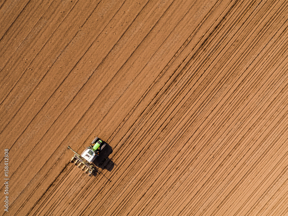 Aerial shot of a farmer seeding, sowing crops at field. Sowing is the process of planting seeds in the ground as part of the early spring time agricultural activities.