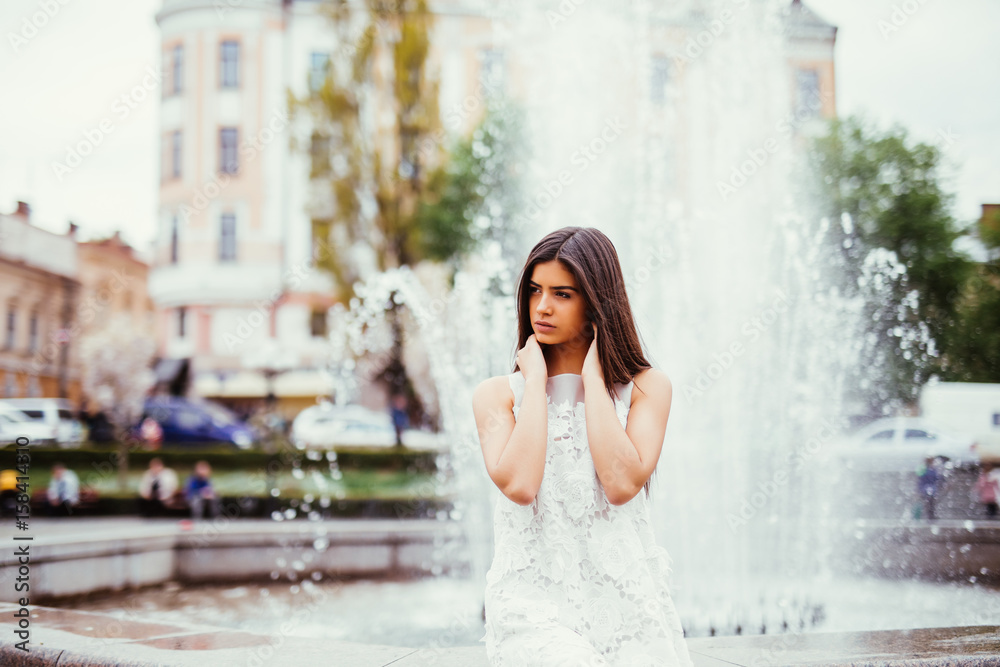 Young beautiful stylish girl walking and posing in city near fountains. Outdoor summer portrait of young classy woman