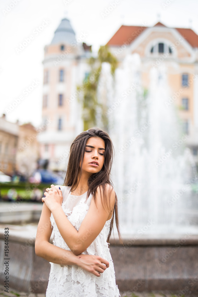 Young caucasian female standing near fountain. Close-up portrait woman outdoor.